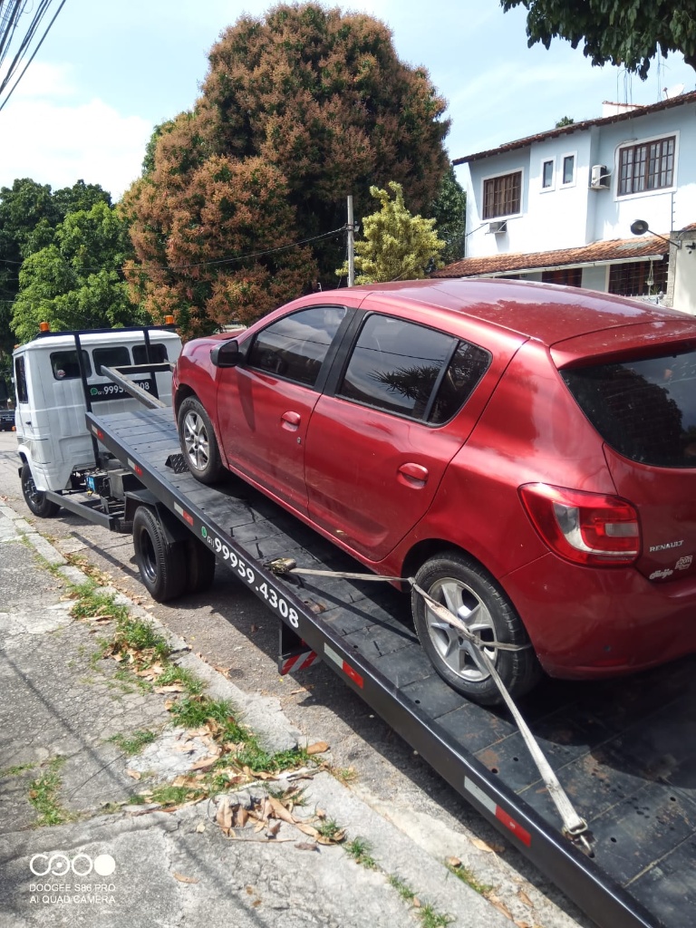 Carro vermelho sendo rebocado em uma rua residencial.